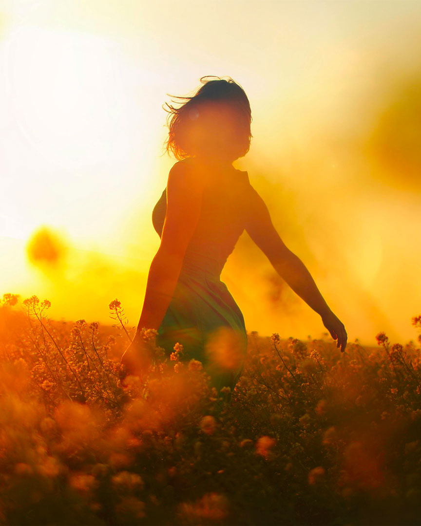 femme de dos dans un champ au coucher du soleil